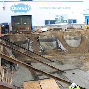 Gleich Anfang Januar wurde die Baugrube ausgeweitet, so dass die Regenwasser-Zisternen kurzfristig wieder zu sehen waren. Mit den T-Trägern wird die Wand zum Grundstücknachbar abgestützt. Erste Teile der Bodenplatte wurden betoniert,…